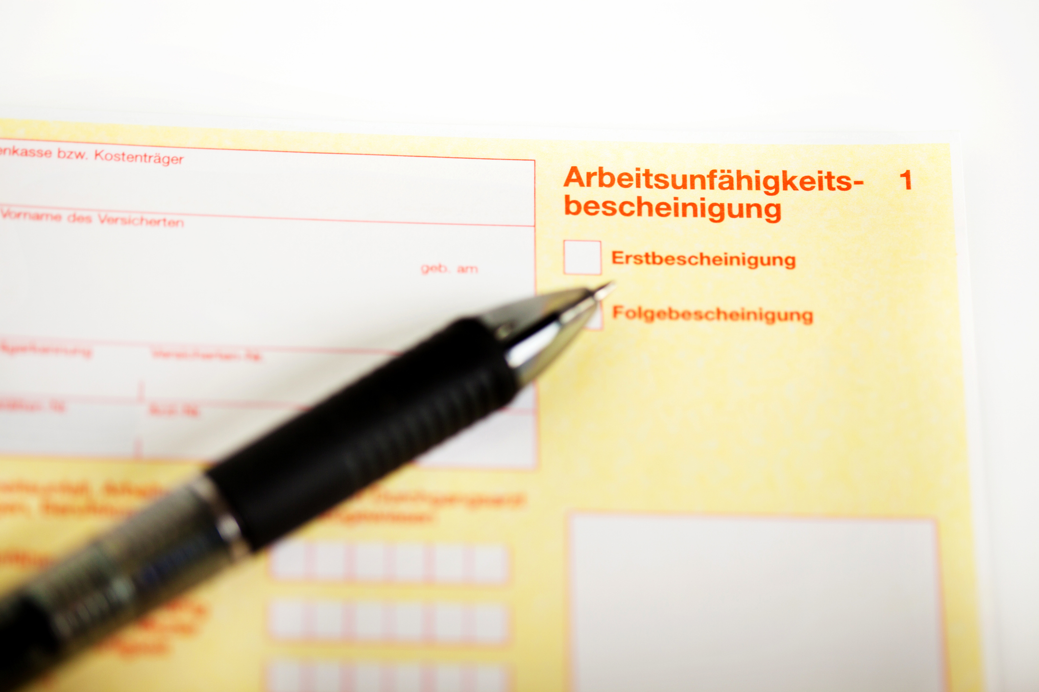 Eine Arbeitsunfähigkeitsbescheinigung mit einem darauf liegenden Stift.